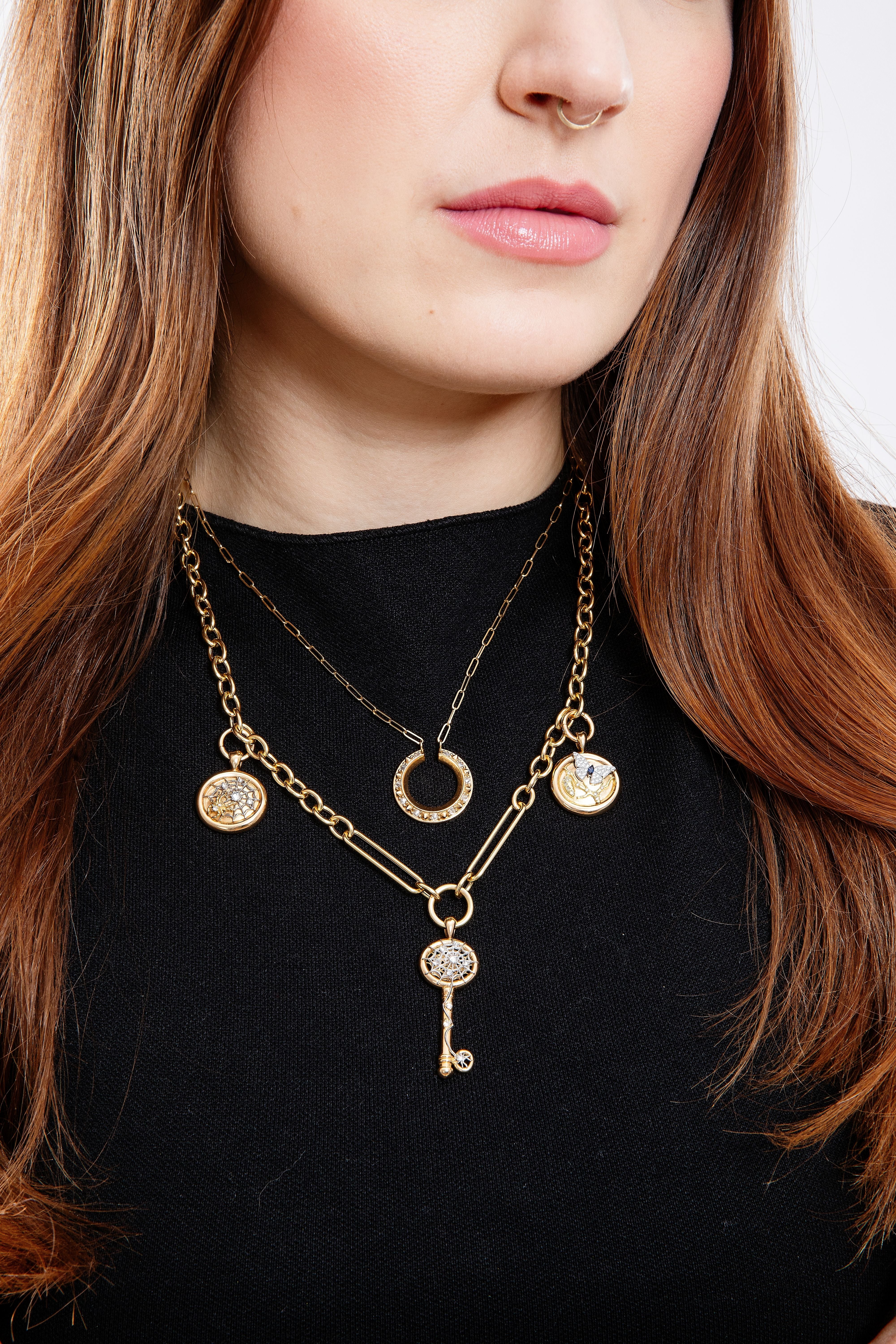 A model wearing a black top to highlight the 18k gold pendants & charms styled on the 18” ‘Olivia’ yellow gold chain.