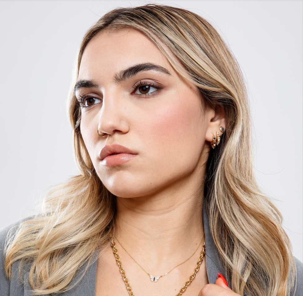 A model wearing various 18k yellow gold, diamond, and precious gemstone necklaces, hoops, and stud earrings designed by Ana-Katarina Fine Jewelry.