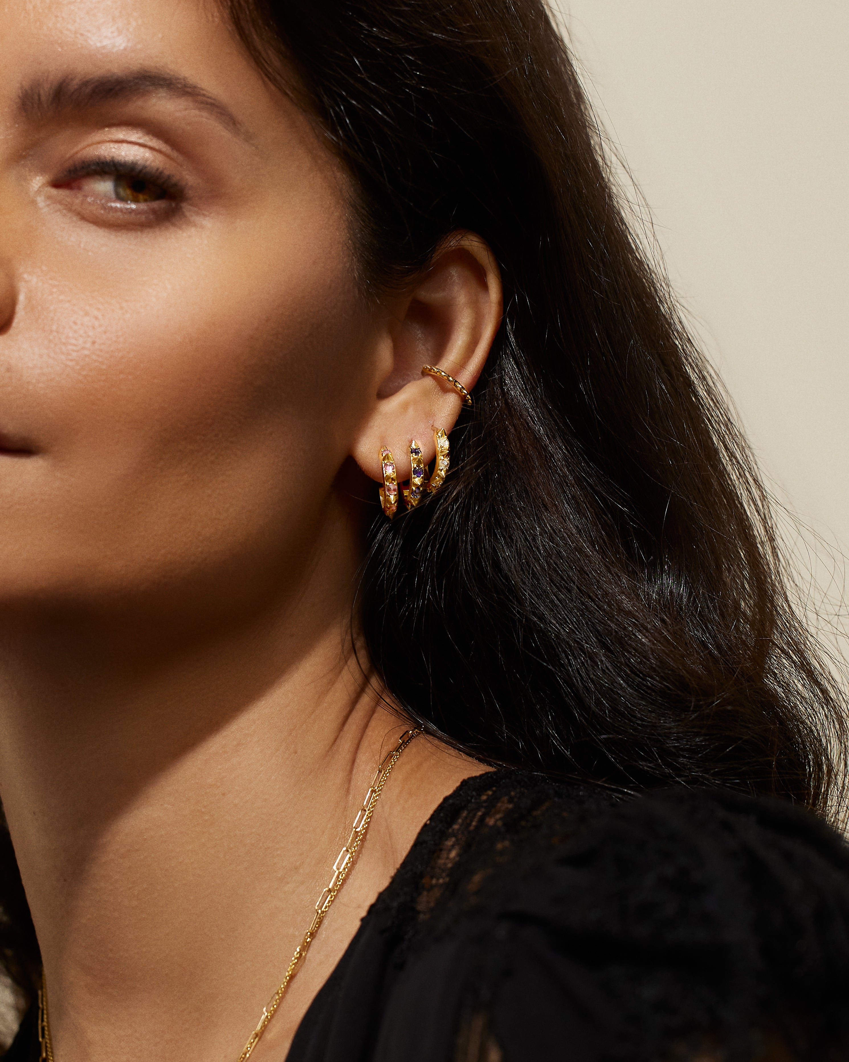 A model wearing the 'Attitude' Valerie Pink Sapphire Mini Hoops in pink and yellow, crafted with 18k yellow gold and adorned with inverted Pink Sapphires and gold spikes, they're a reinvented classic mini gold hoop earring.