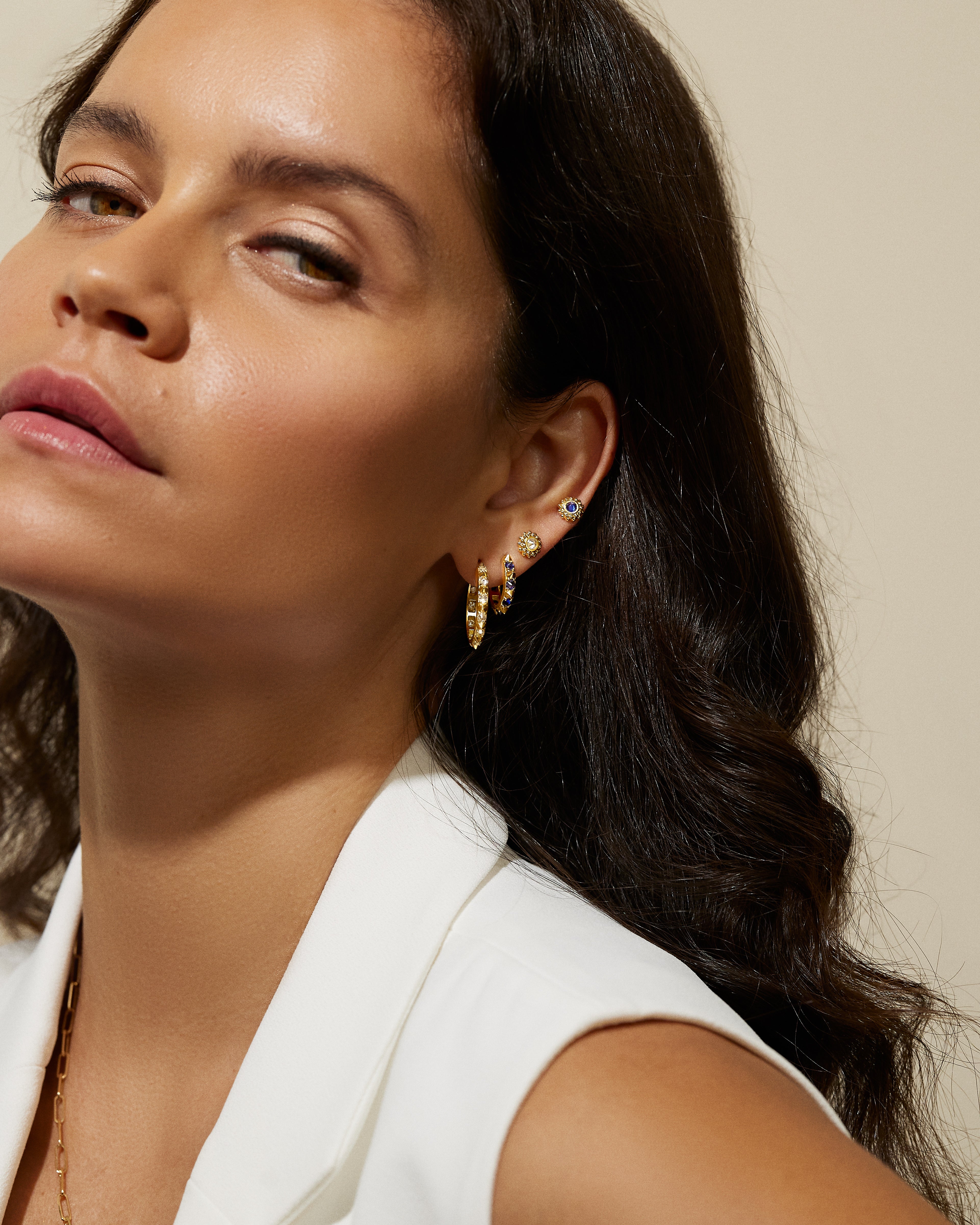 A model wearing various hoops and stud earrings in 18k yellow gold, diamonds, and garnets all designed by Ana-Katarina Fine Jewelry.