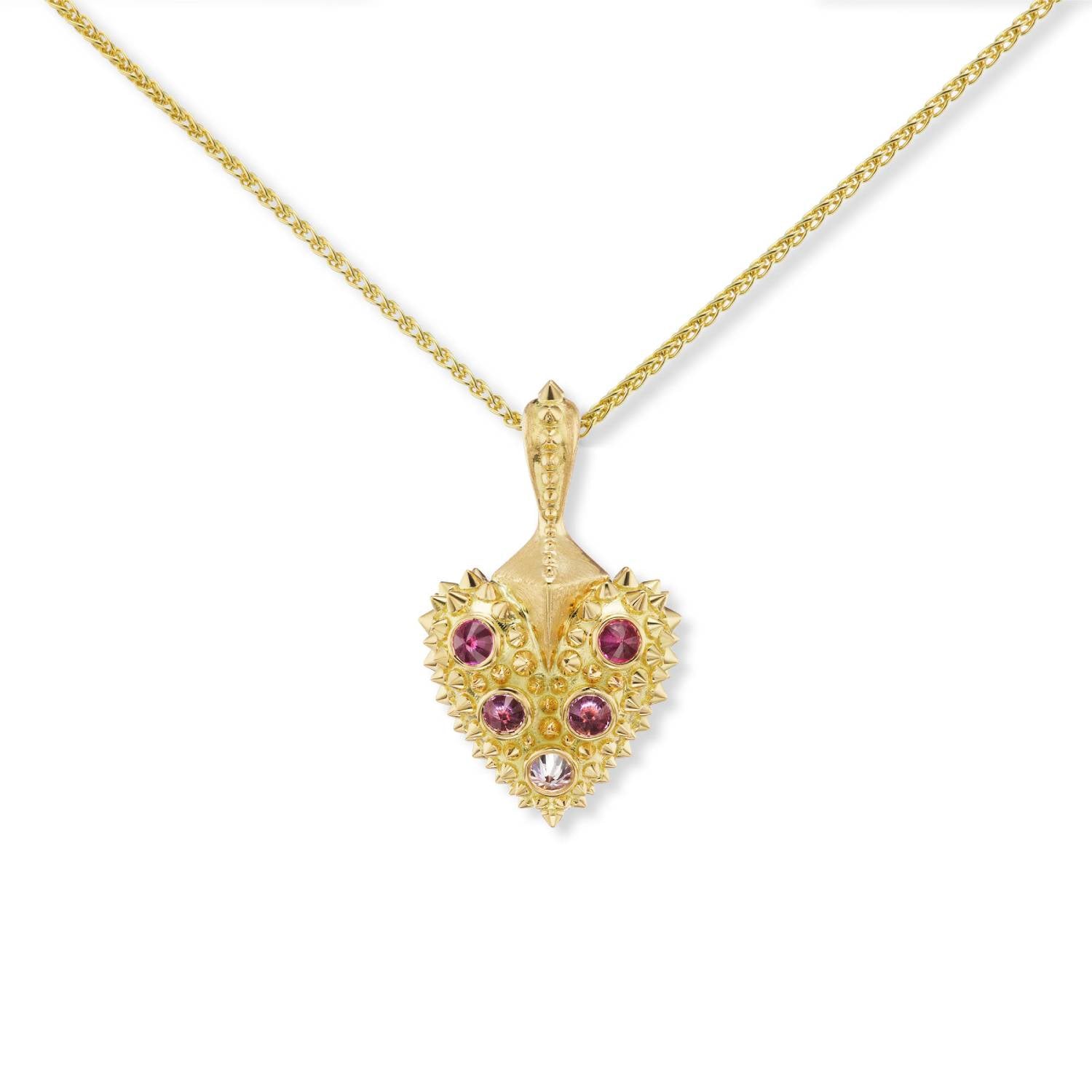 A closeup view of an 18k gold heart with inverted pink sapphires & diamond with 18k yellow gold spikes on a 2mm yellow gold chain - designed by Ana-Katarina fine jewelry.