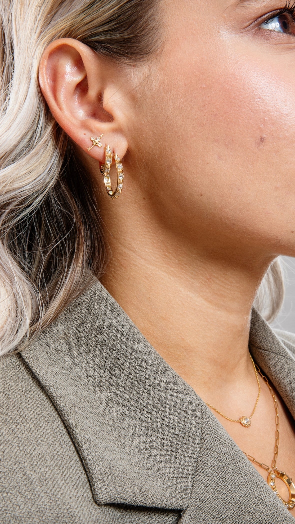 A model wearing five pieces of 18k yellow gold fine jewelry from Ana-Katarina's Attitude collection - the ‘Valerie’ Diamond Mini Hoop Earring in large and small are styled a gold cross stud earring by Ana-Katarina Fine Jewelry. .
