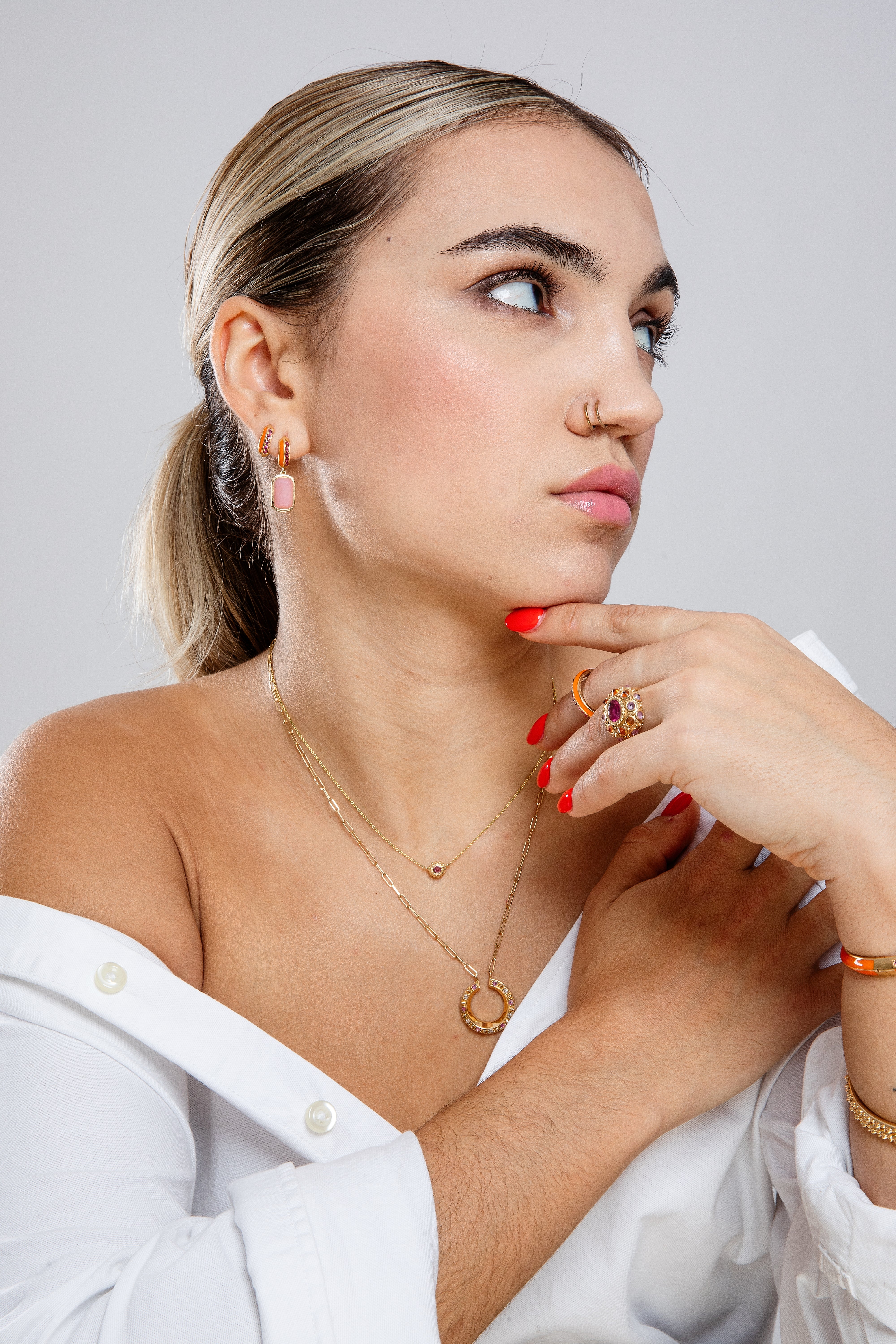 A person looking away from the camera modeling 18k gold and pink tourmaline fine jewelry, featuring the 'Sweet, Happy Life' Huggies earrings with .48tw pink tourmaline and orange enamel from Ana-Katarina's Attitude 'Sweet Happy Life' collection & other fine 18k gold chains and bangles.