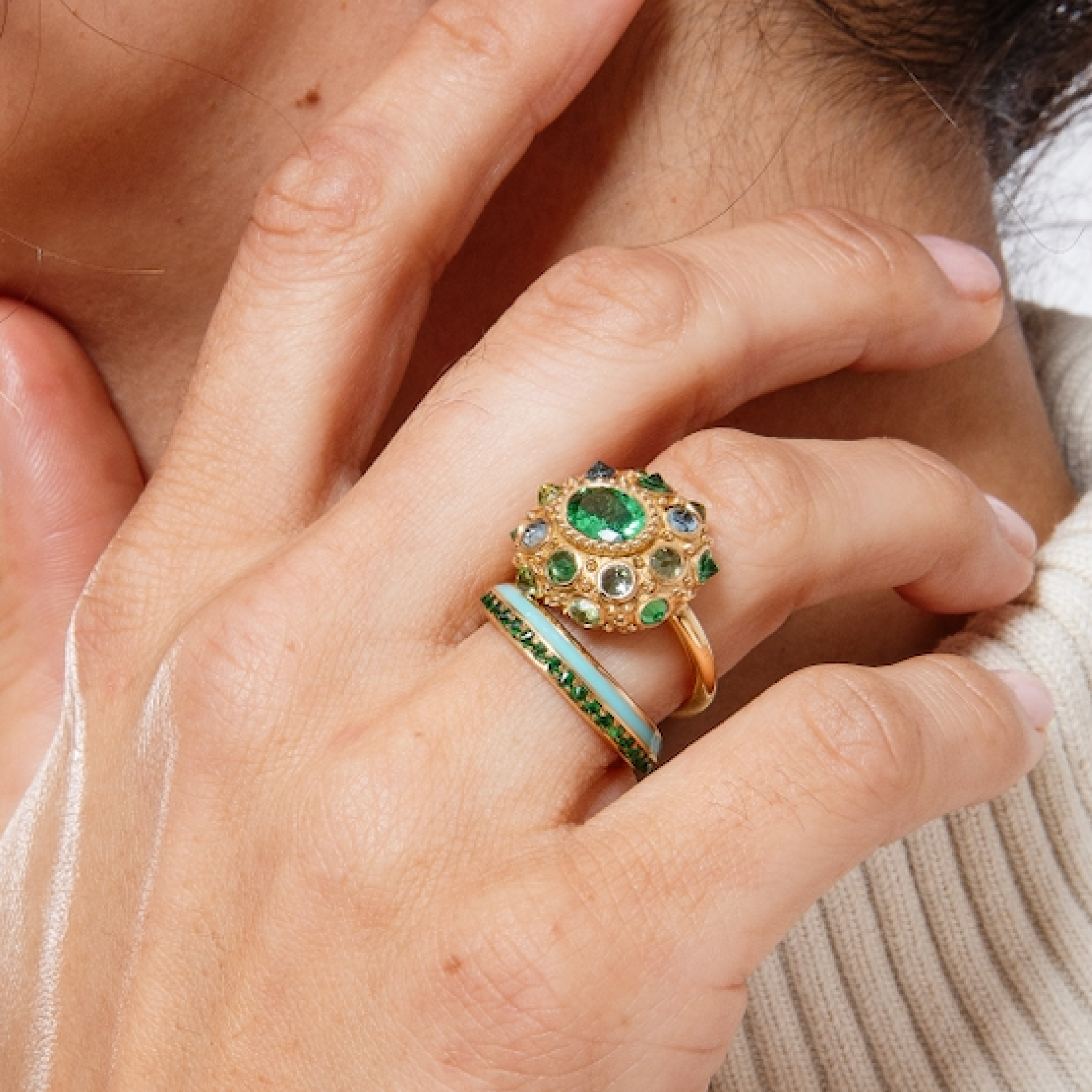 A model wearing two 18K yellow gold rings designed by Ana-Katarina featuring a vibrant arrangement of Tsavorite Garnets, Aquamarines & Peridot in the colors of blue & green creating a captivating & colorful display.