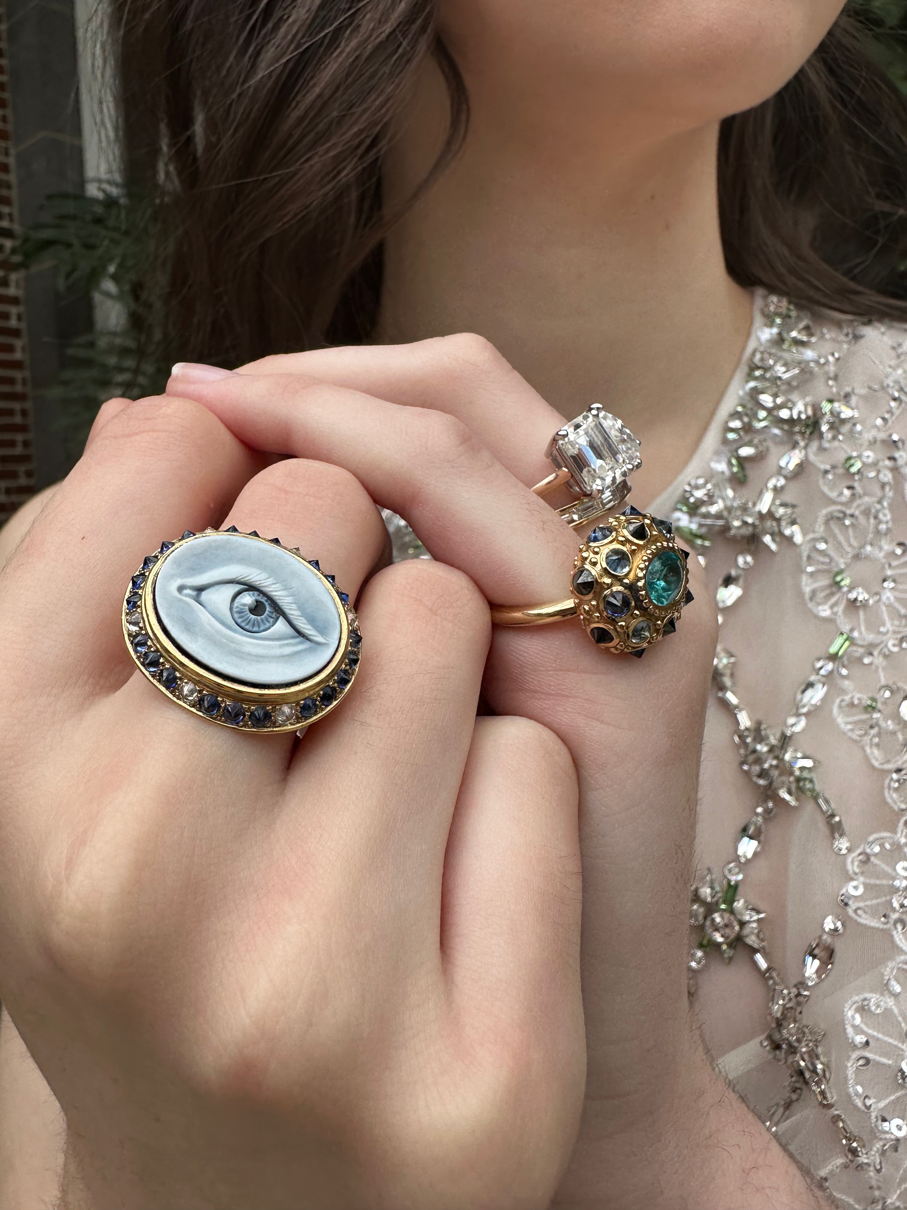 A closeup of a model's hands showcasing this stunning ring crafted in 18k yellow gold, adorned with Apatite, Blue Sapphires, and Black Diamonds, featuring an exquisite design inspired by the sea urchin. 