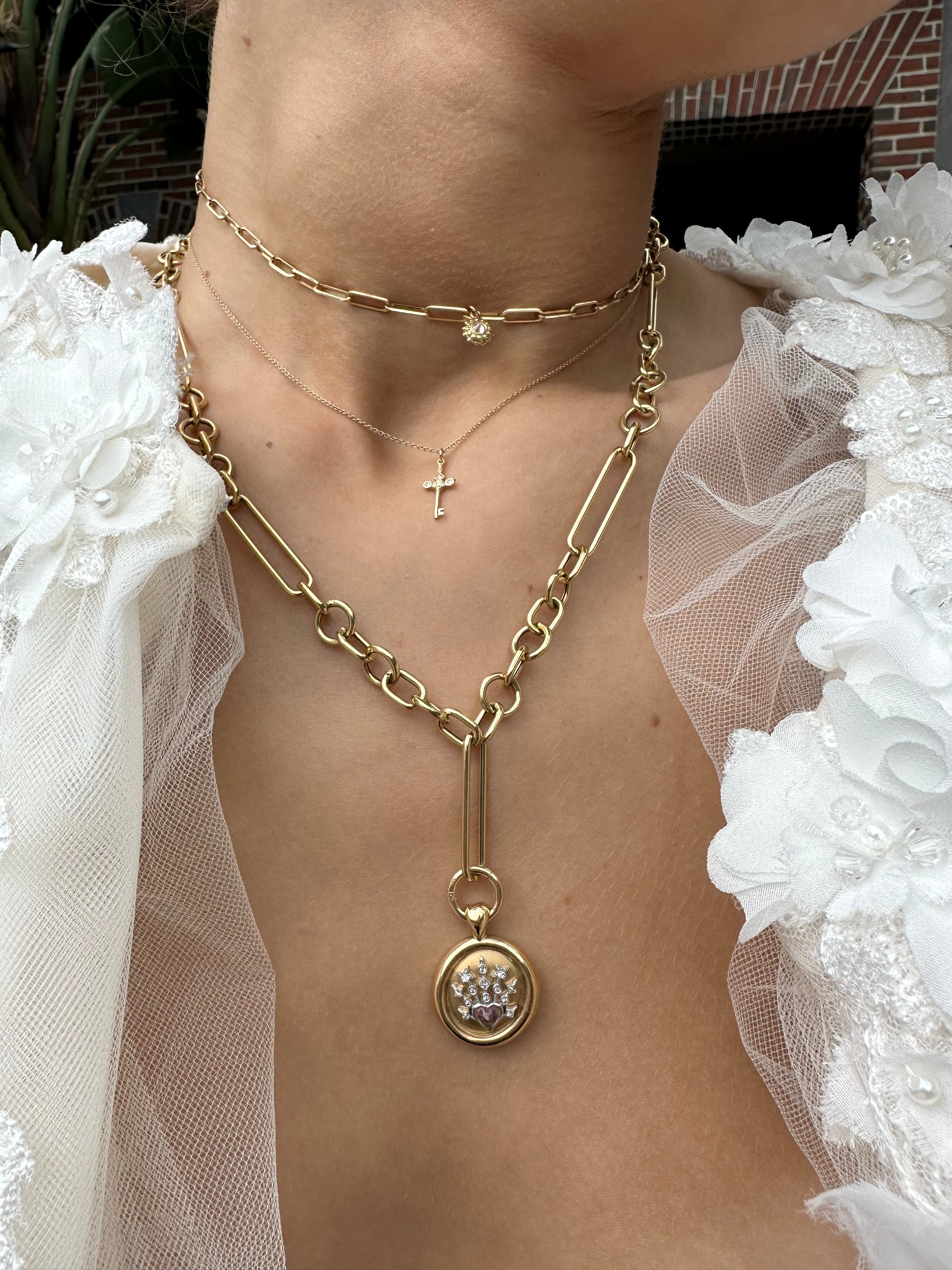 A model wearing three gold chain with interchangeable pendants and charms added using ‘Charm-ing’ Link-style charm holders designed by Ana-Katarina Fine Jewelry. Sunburst diamond pendants with inverted diamonds, a small gold cross, and a diamond pendant hang from the gold chains - all gold chains, gold pendants, and gold charms designed by Ana-Katarina. 