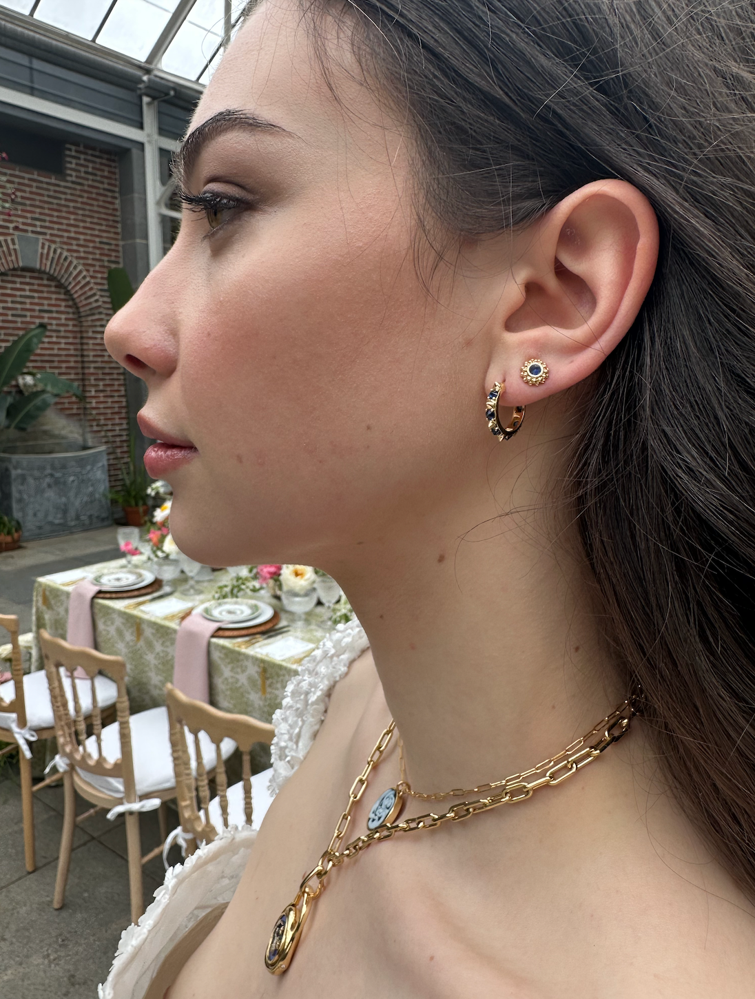 A person modeling the 'Attitude' Valerie Blue Sapphire Mini Hoops in blue and yellow, crafted with 18k yellow gold and adorned with inverted blue sapphire and gold spikes, they're a reinvented classic mini gold hoop earring.