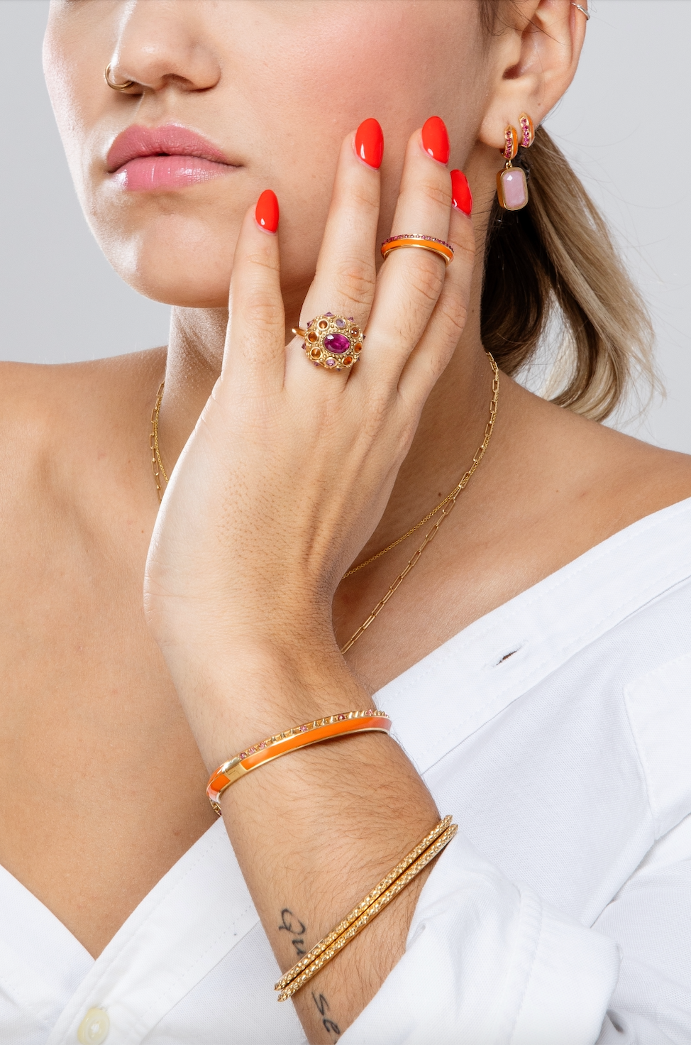 A close-up of a person wearing Ana-Katarina Attitude 'Sweet Little Life' 18k yellow gold & pink tourmaline jewelry with orange enamel. A close-up of a person wearing fine jewelry in pink and orange from the Attitude 'Sweet Little Life' 18k yellow gold & pink tourmaline collection with orange enamel accents. Designed by Ana-Katarina Fine Jewelry.