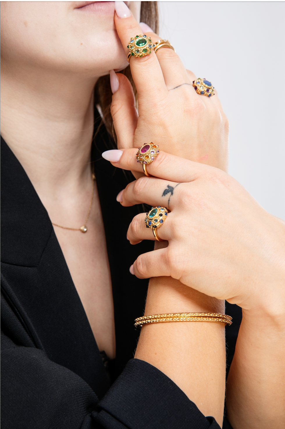 A close-up view of a person wearing all four of Ana-Katarina's signature 18k yellow gold & inverted precious gemstones rings - all inspired by the sea urchin. 