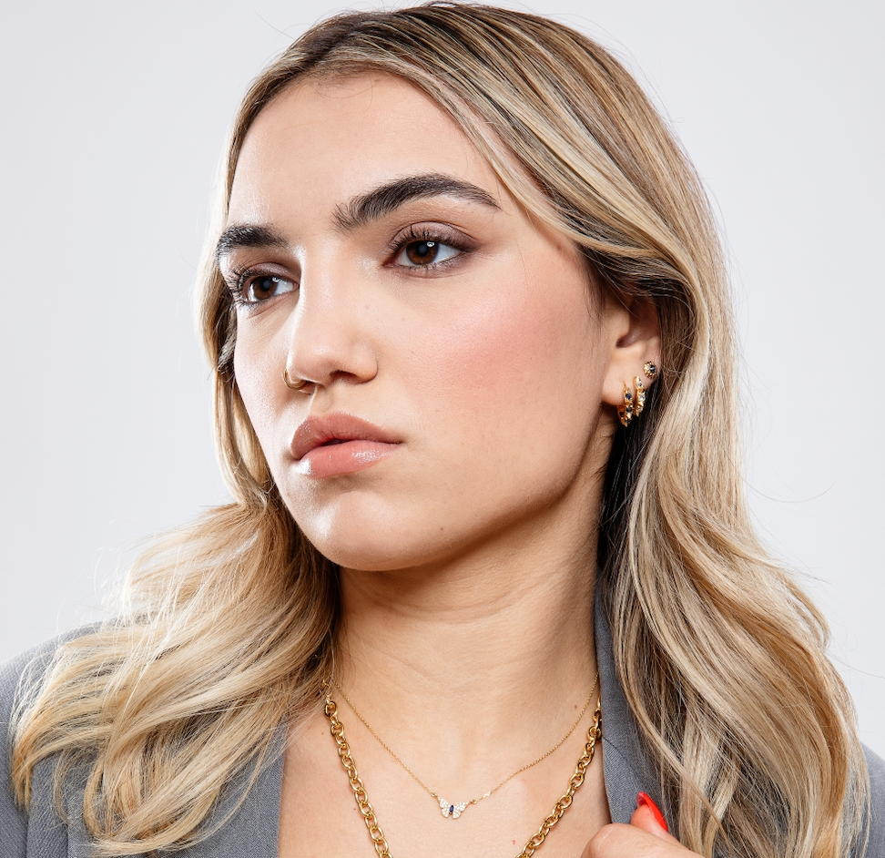 A model wearing various 18k yellow gold, diamond, and precious gemstone necklaces, hoops, and stud earrings designed by Ana-Katarina Fine Jewelry. 
