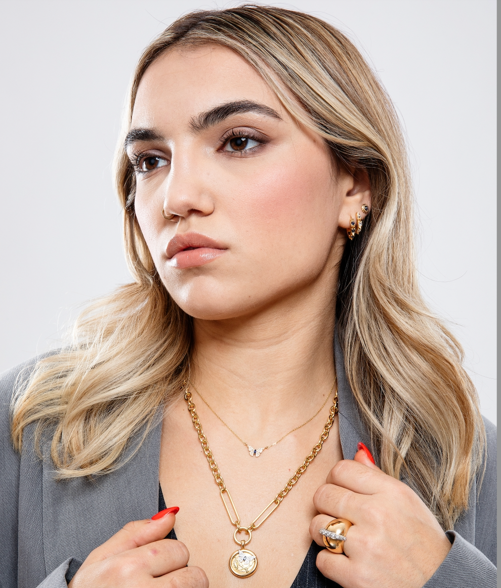 A model wearing six pieces of Ana-Katarina's 18k yellow gold fine jewelry - the Attitude ‘Valerie’ Diamond Mini Hoop Earrings are styled with two additional sets of earrings and two 18k yellow gold necklaces from Ana-Katarina Fine Jewelry. 