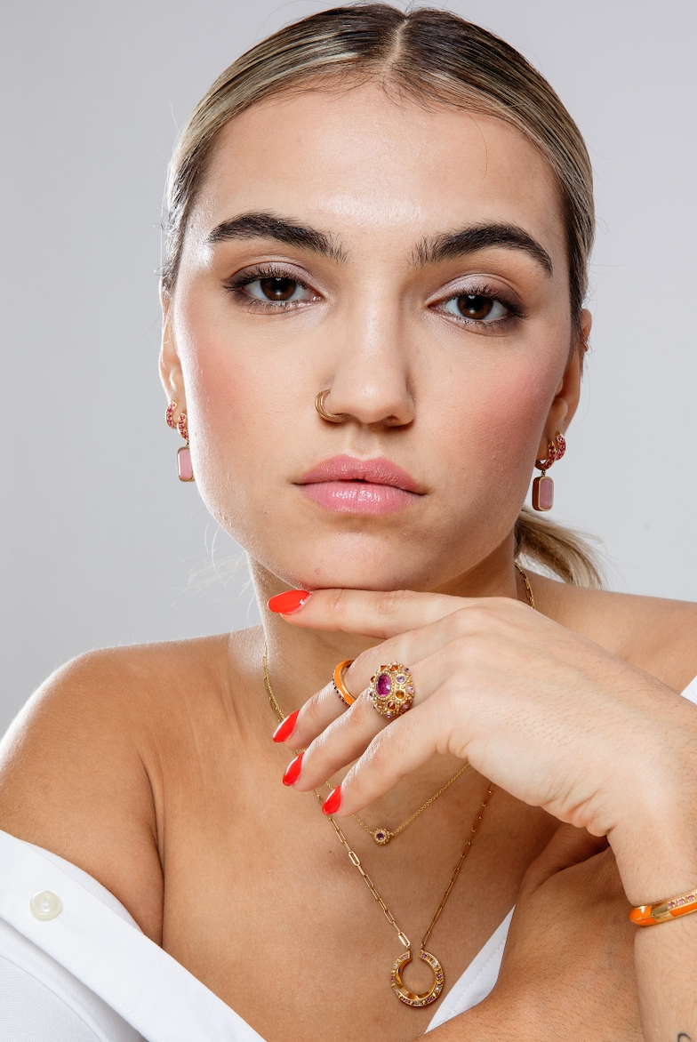 A person wearing an exquisite 18K yellow gold and precious gemstone ring designed by AnaKatarina Fine Jewelry. Adorned with inverted Rhodalite Garnets, Pink Sapphires, and Orange Sapphires this playfully stunning ring features a large, captivating diamond-cut pink sapphire in the center as its focal point.