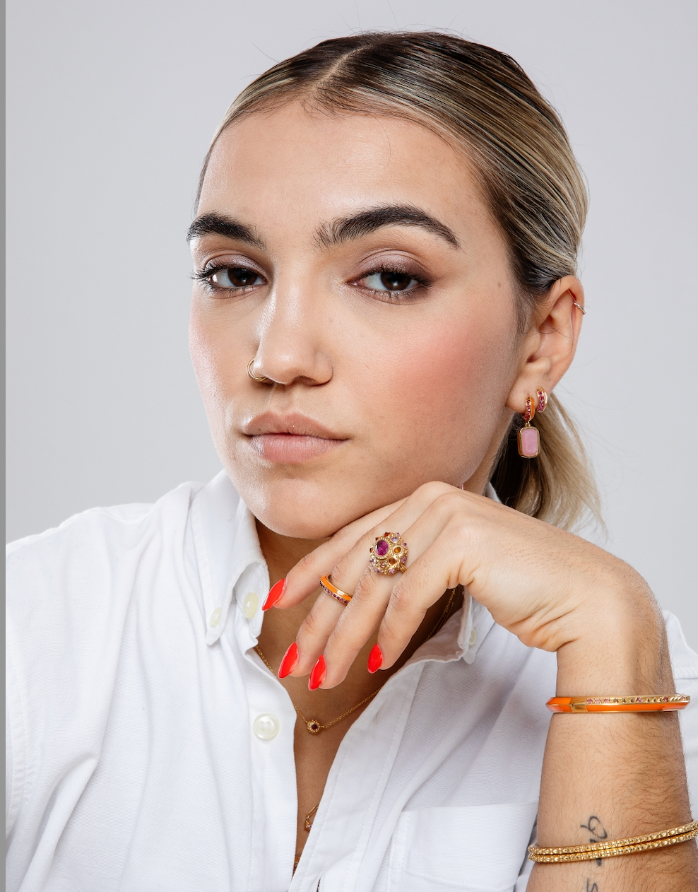 A person modeling fine jewelry in pink and orange from the Attitude 'Sweet Little Life' 18k yellow gold & pink tourmaline collection with gold spikes and orange enamel accents. Designed by Ana-Katarina Fine Jewelry.