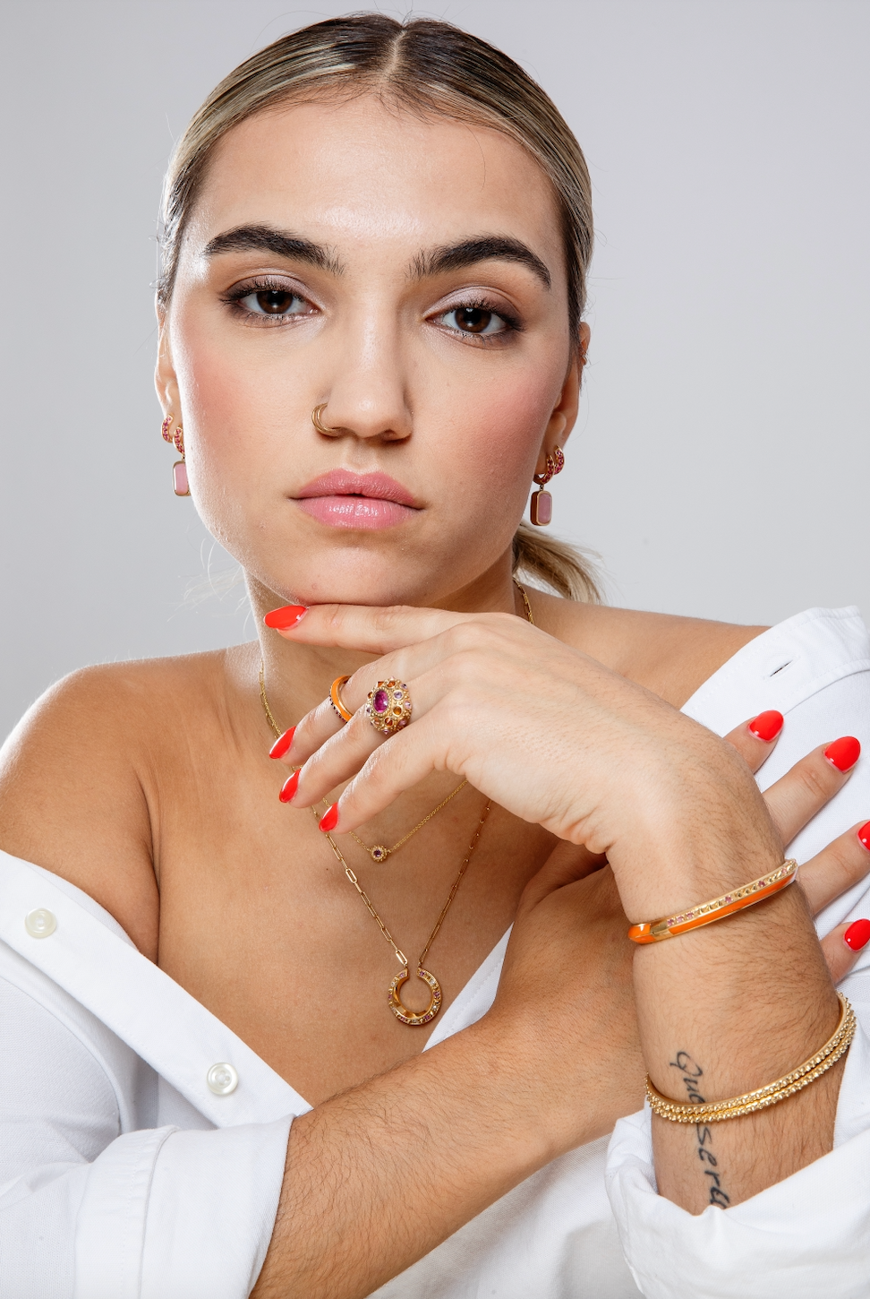 A person looking straight at the camera while modeling fine jewelry in pink and orange from the Attitude 'Sweet Little Life' 18k yellow gold & pink tourmaline collection with gold spikes and orange enamel accents. Designed by Ana-Katarina Fine Jewelry.
