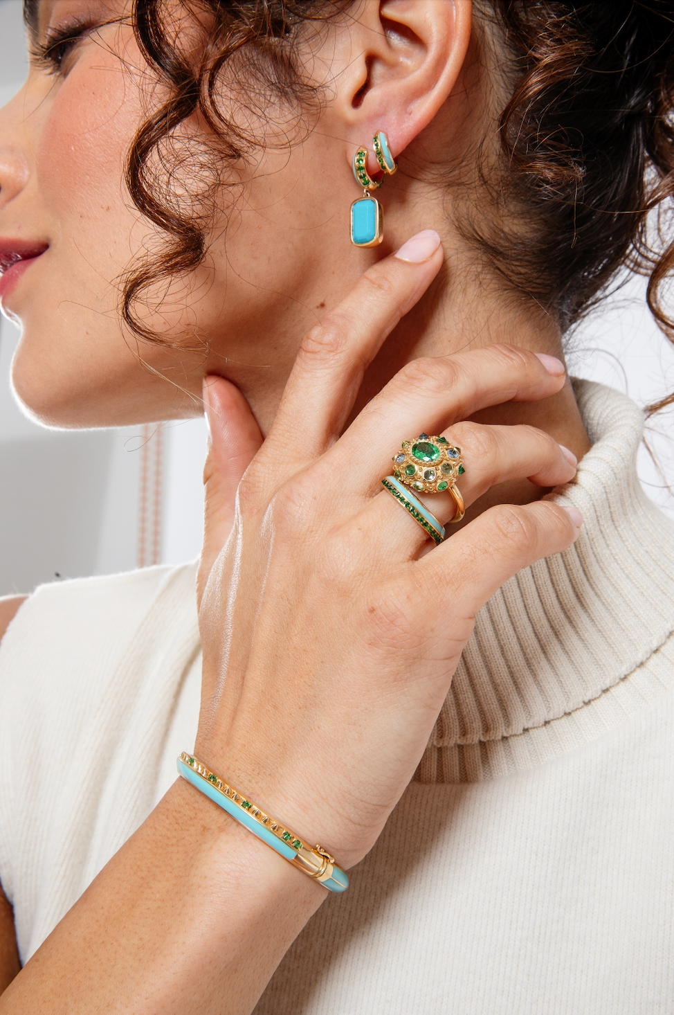 A person modeling the lavish 'Sweet, Happy Life' Tsavorite Garnet Stacking Ring designed by Ana-Katarina Fine Jewelry, while showcasing other fine jewelry from the collection with a captivating combination of green, turquoise, and gold hues, adorned with Tsavorite Garnets and Turquoise Enamel details. 
