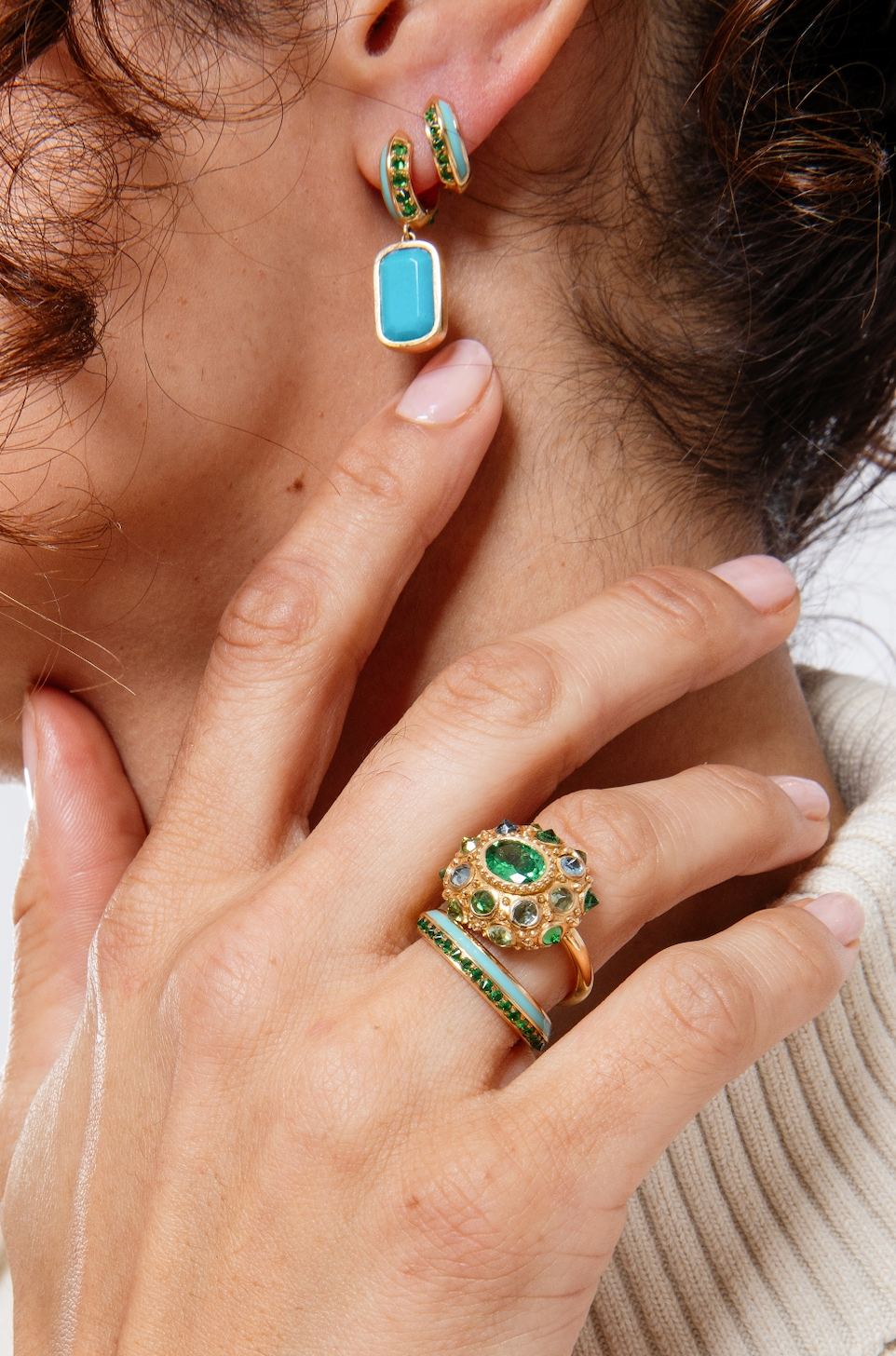 A closeup of a model wearing the lavish 'Sweet, Happy Life' Tsavorite Garnet Stacking Ring designed by Ana-Katarina Fine Jewelry, showcasing other fine jewelry from the collection with a captivating combination of green, turquoise, and gold hues, adorned with Tsavorite Garnets and Turquoise Enamel details. 