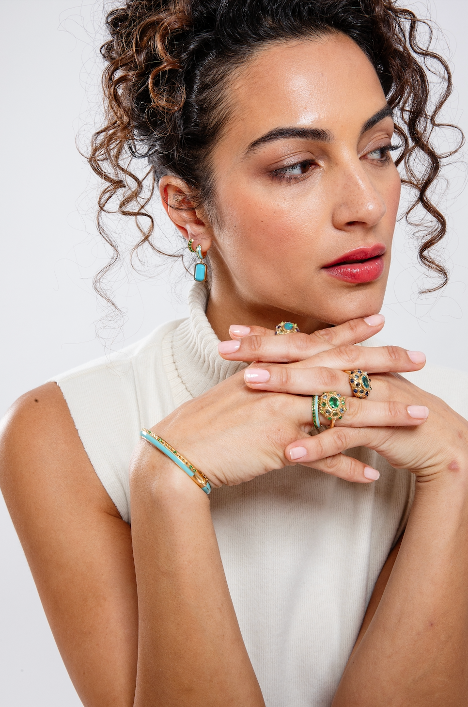 A person wearing the 'Sweet, Happy Life' Tsavorite Garnet Huggie Earrings designed by Ana-Katarina Fine Jewelry while showcasing other fine jewelry from the collection with a captivating combination of green, turquoise, and gold hues, adorned with Tsavorite Garnets and Turquoise Enamel details. 