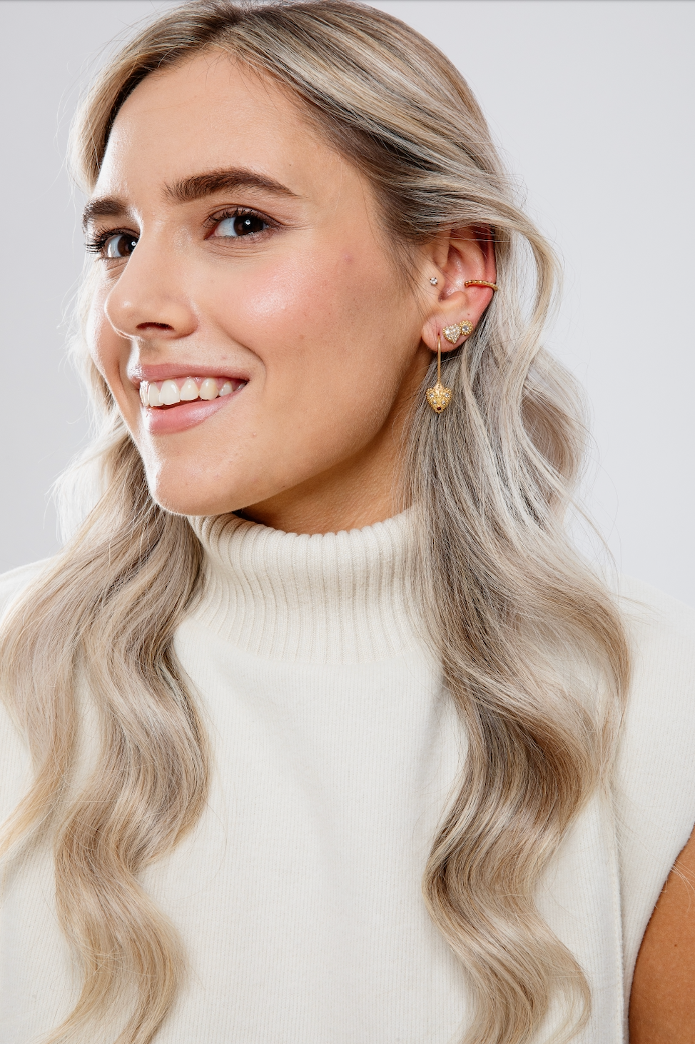 A model smiling while wearing various 18k yellow gold & inverted diamond & ruby spike drop & stud earrings from Ana-Katarina’s ‘Pierce Your Heart’ collection.