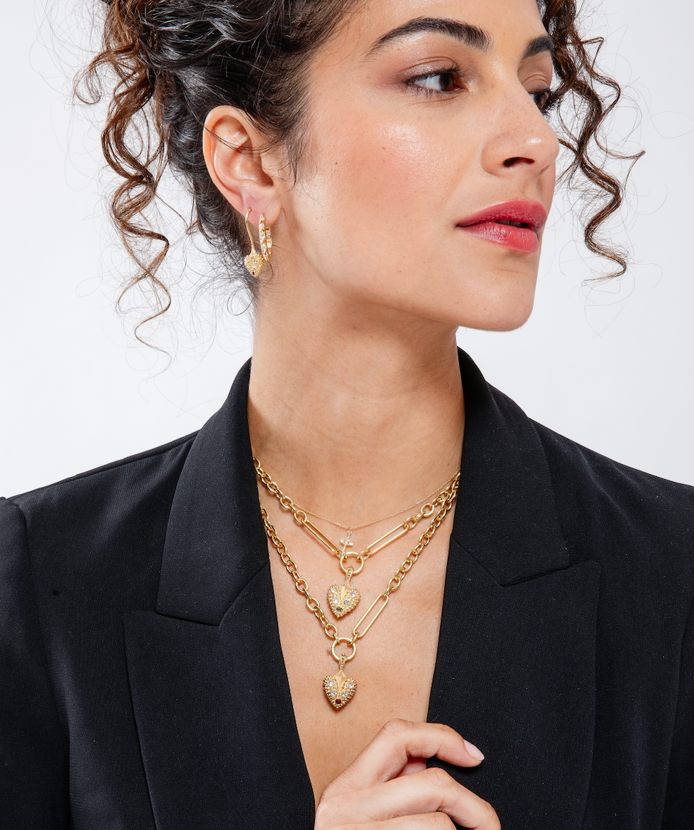 A model with dark curly hair wearing two of Ana-Katarina’s bleeding heart pendants on large 18k yellow gold chains as well as other spiked heart rings and earrings from the ‘Pierce Your Heart’ collection. 
