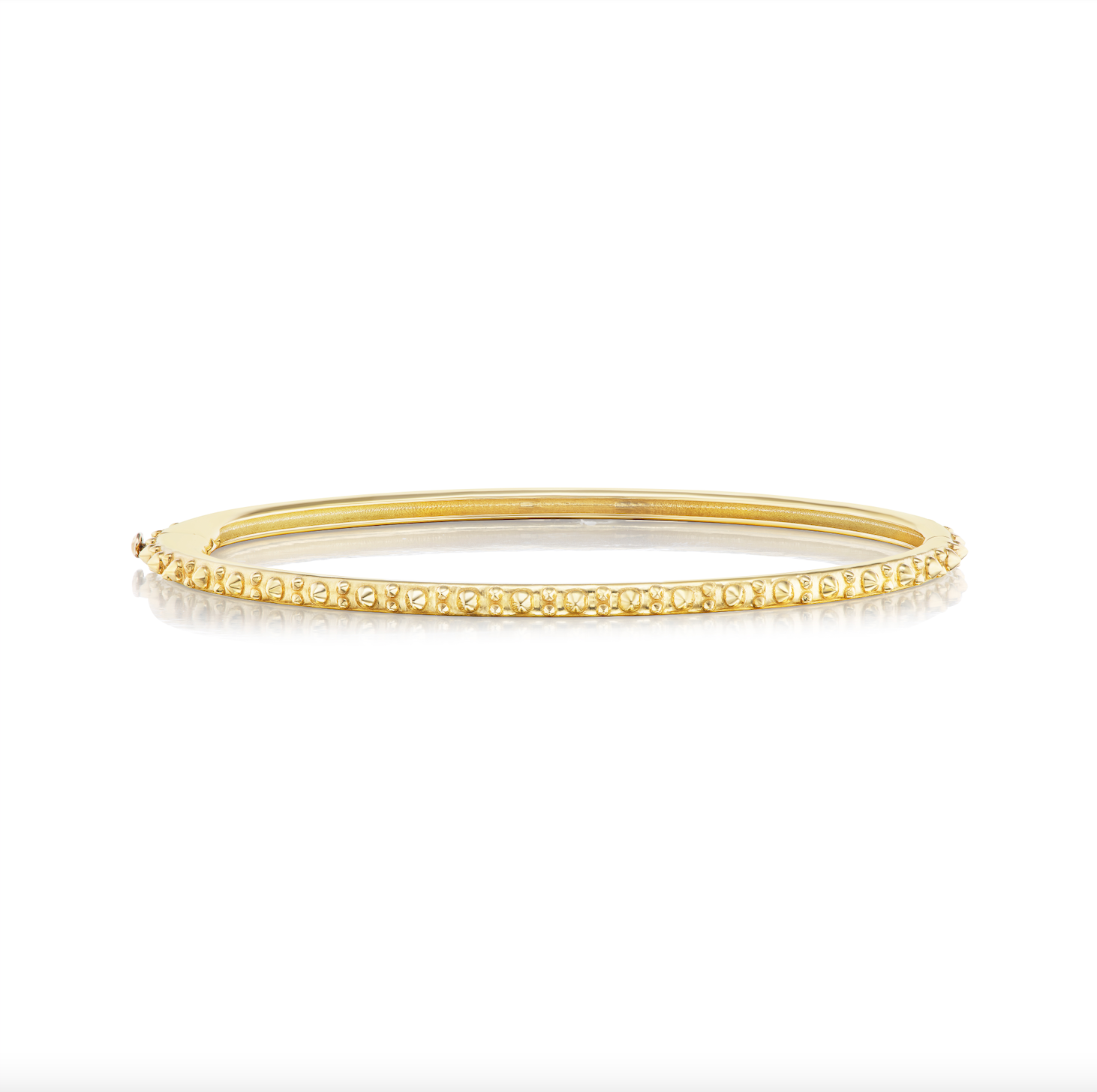 A side view of AnaKatarina's Attitude Yellow Gold 'Adrina Loves a Bangle' 18K yellow gold bangle. In her reinvention of the classic bangle, AK combines traditional form with a fusion of confidence and femininity, showcasing luxurious 18k gold spikes.