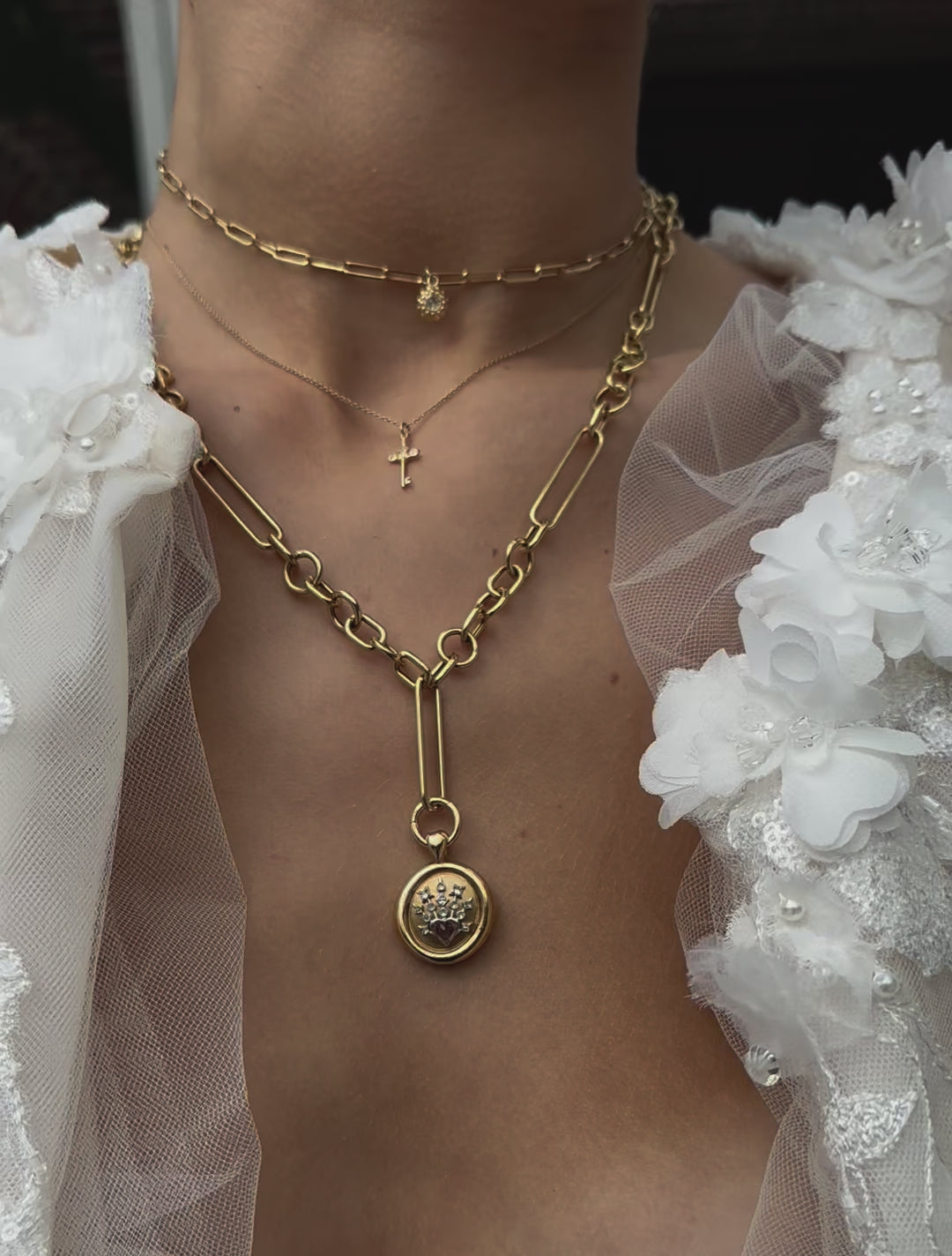 A close-up video of a model wearing various unique fine jewelry from Ana-Katarina’s designer collections. All in 18k yellow gold and diamonds: a small gold cross on a fine cable chain, a sea urchin design on a small paperclip chain worn as a choker, and along chunky gold chain with a large gold and diamond pendant.