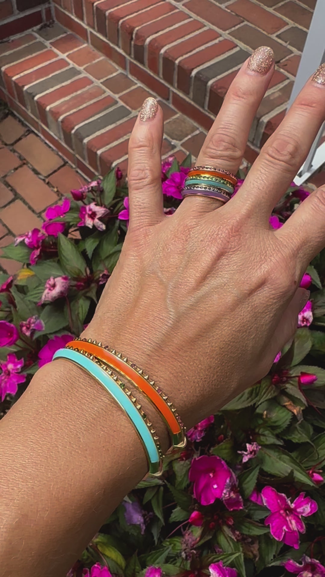 A video of a person modeling the 'Sweet, Happy Life' Tsavorite Garnet stacking bangle and the Pink Tourmaline Bangle with matching stacking rings - all designed by AnaKatarina Fine Jewelry and crafted from 18k Yellow Gold and embellished with .48tw Tsavorite Garnet and Turquoise Enamel.