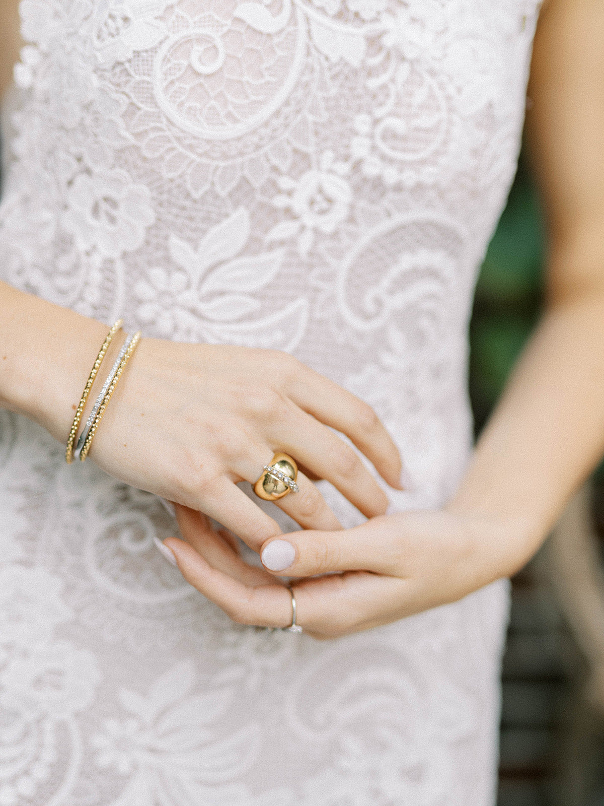 A closeup of the hands of a person wearing a white dress and modeling the AnaKatarina signature ring: the AK Attitude Ring. A luxurious 18k yellow gold ring, it is adorned with brilliant .77ct diamonds, embodying the fusion of confidence & femininity.