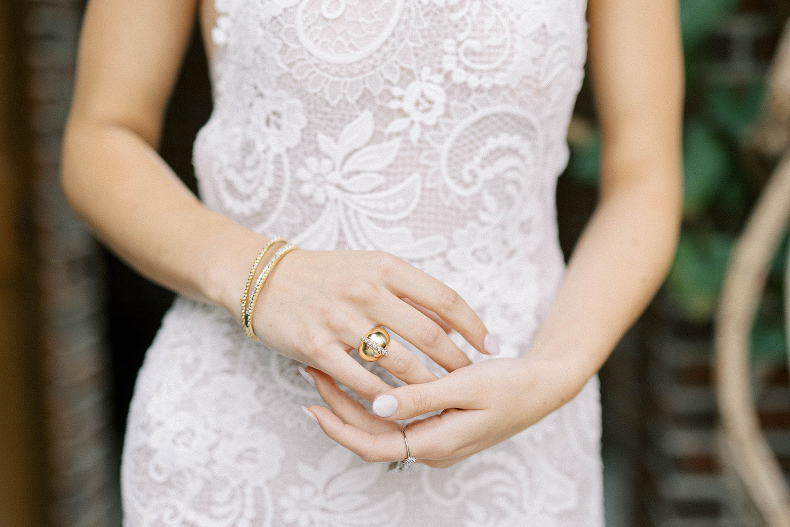 A person wearing a white dress models the AnaKatarina signature ring: the AK Attitude Ring. A luxurious 18k yellow gold ring, it is adorned with brilliant .77ct diamonds, embodying the fusion of confidence and femininity in an elegant and timeless design.