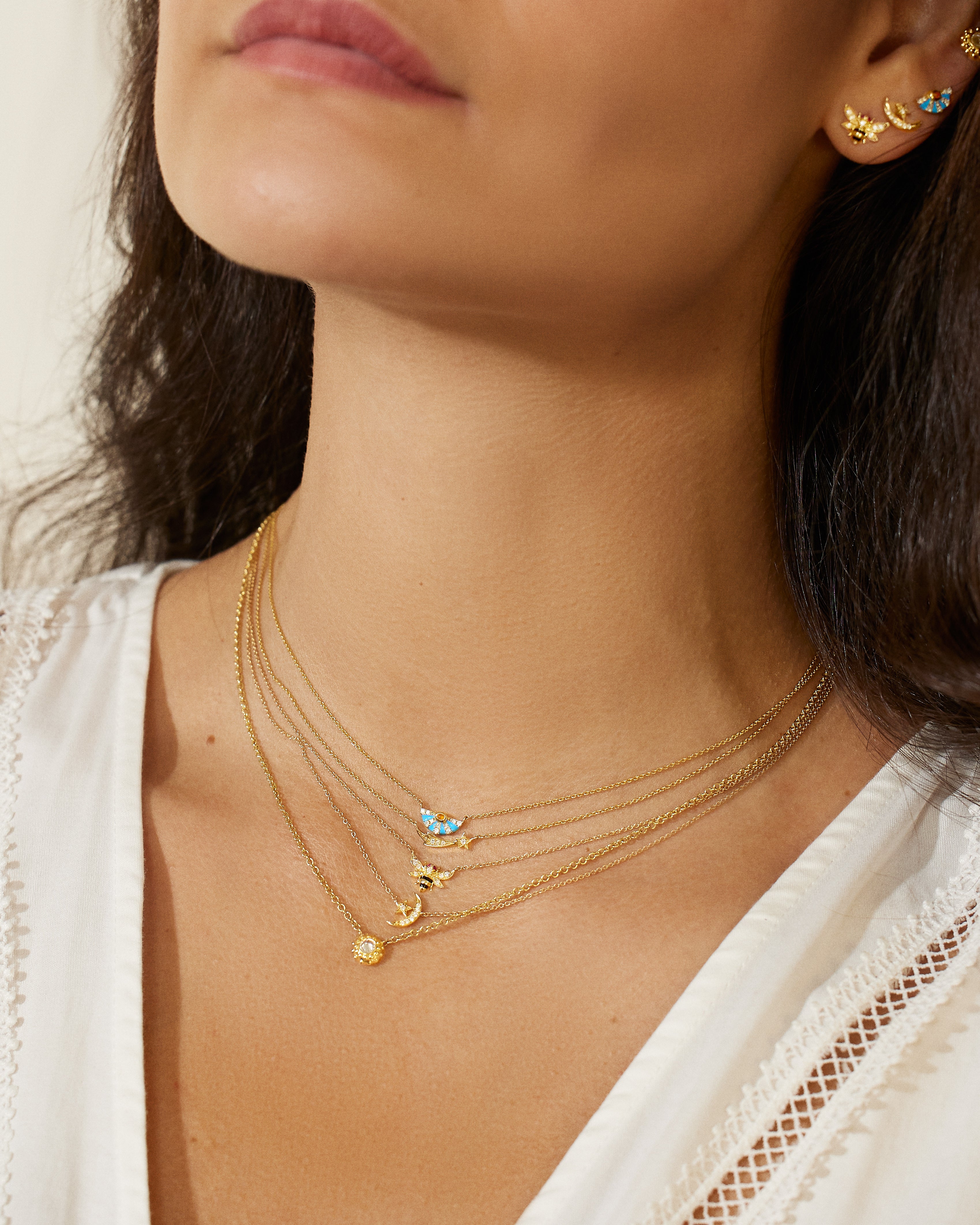 A close-up of a person modeling four necklaces from the AK 4 Elements Collection. One of the center gold necklaces is an 18k Yellow Gold Star & Moon Charm Necklace with .17ct Diamonds on an Elegant Gold Chain.