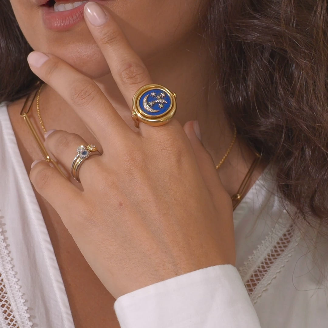 A video of a person showing the versatility of Ana-Katarina's 4 Elements Air Flip Ring in 18k gold, diamonds, and blue enamel featuring the moon and shooting stars on one side and a celestial scene or quantum interconnectivity of the galaxy on the other. 