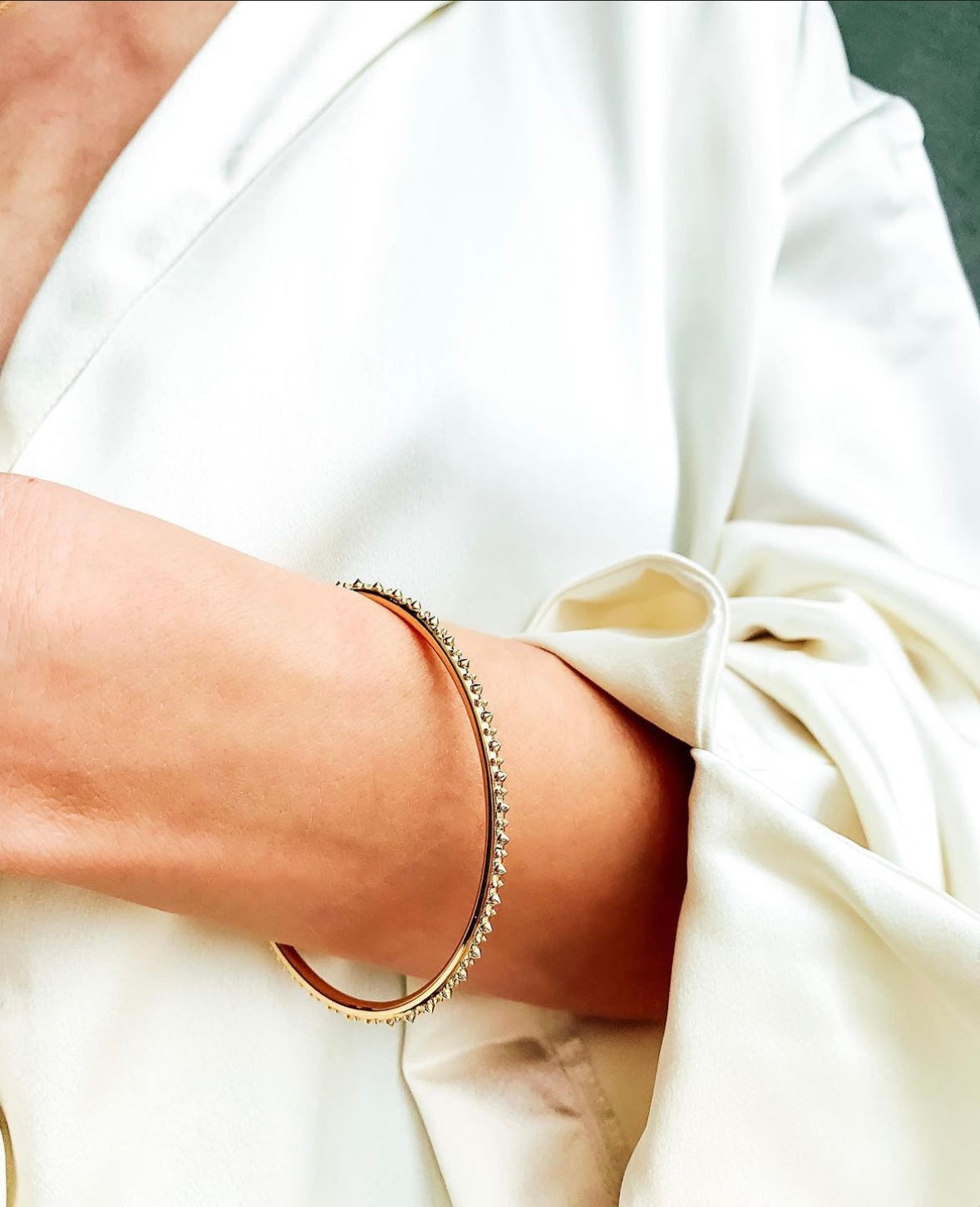 A closeup of the wrist of a model showcasing a side view of AnaKatarina's Attitude White Gold 'Adrina Loves a Bangle' 18K white gold bangle. In her reinvention of the classic bangle, AK combines traditional form with a fusion of quiet class meets edge.