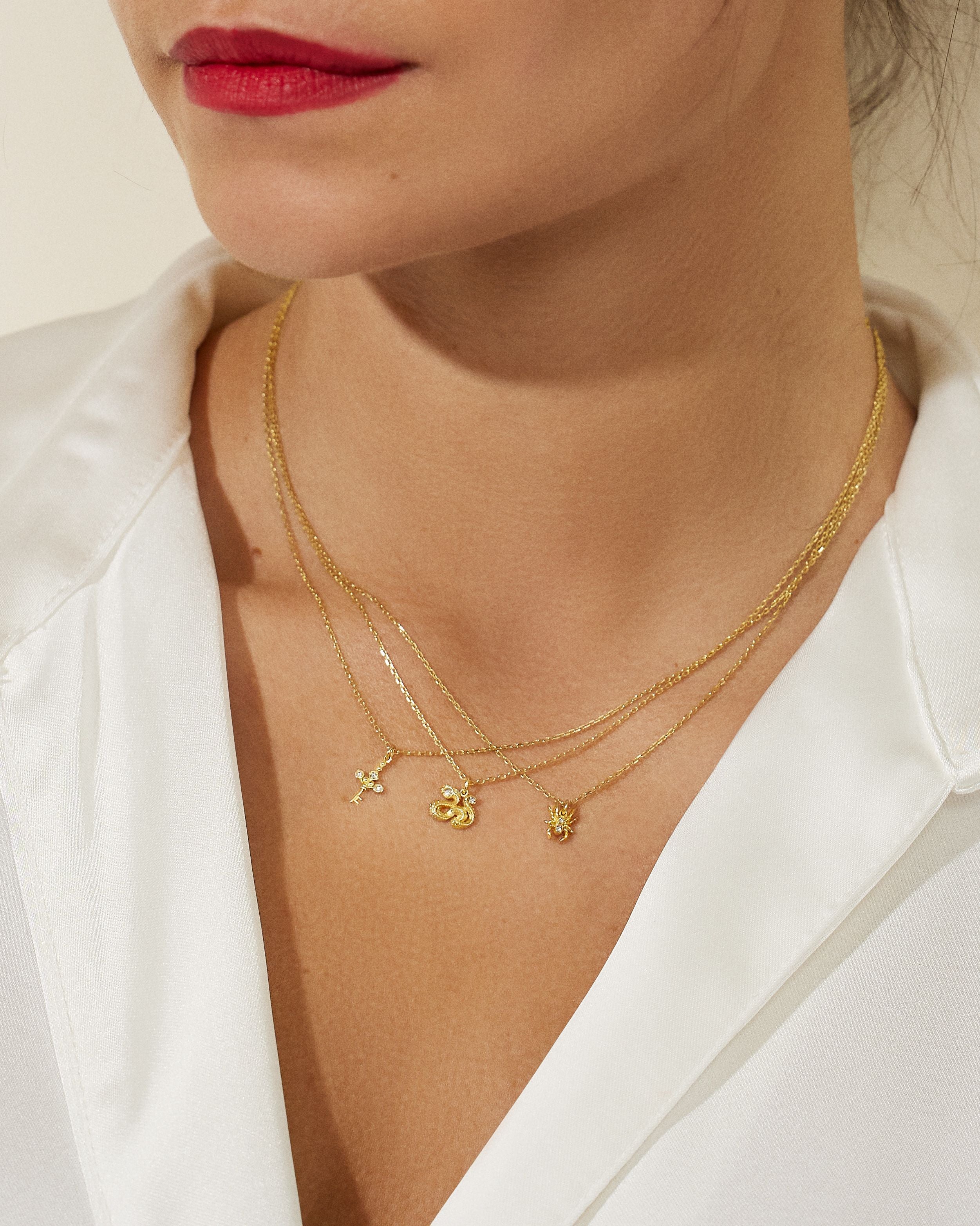 A modeling wearing three 18k yellow gold necklaces from Ana-Katarina fine jewelry’s ‘Impeccable Words’ collection: the North Star Cross, a serpent, and a spider. 