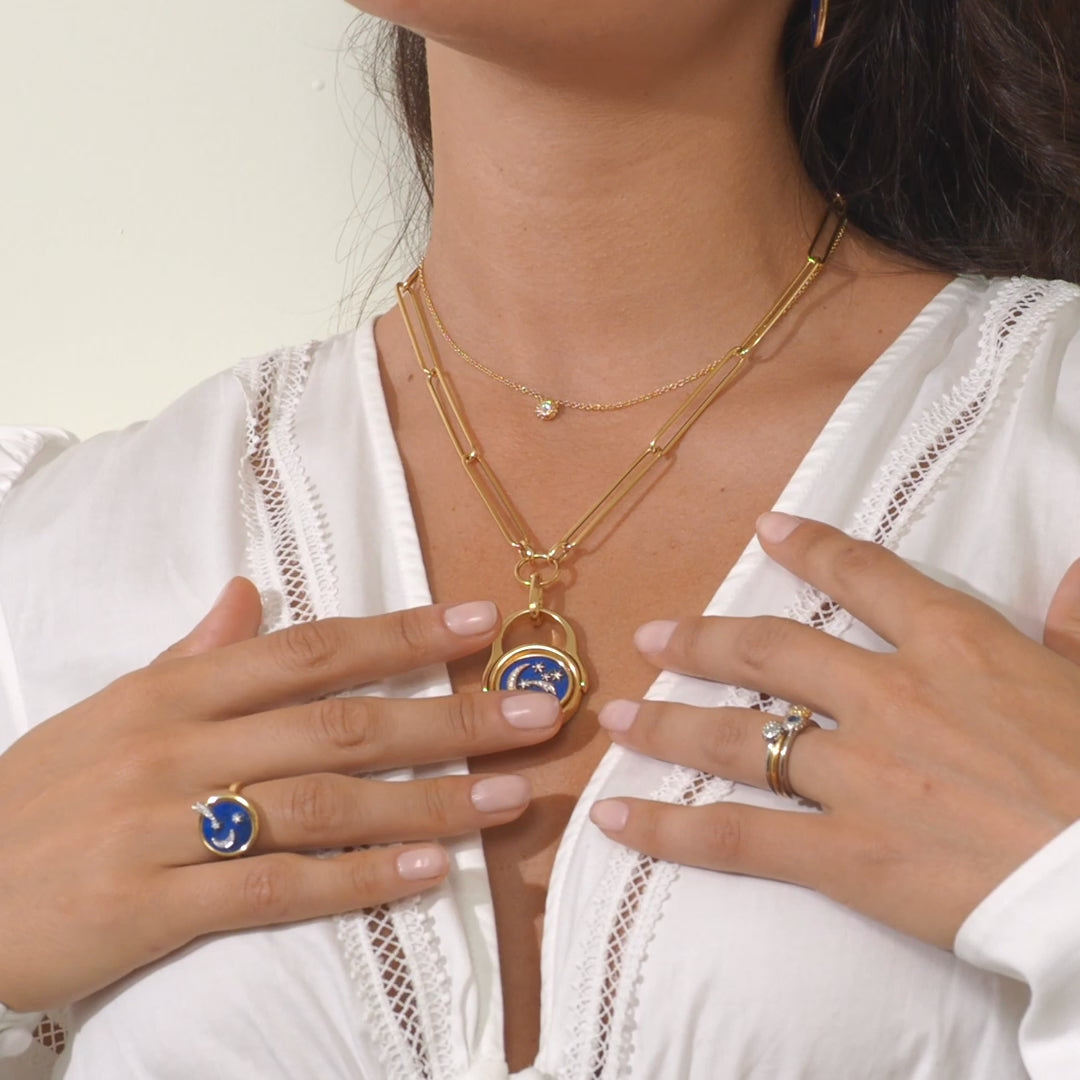 A video of a person showing the versatility of Ana-Katarina's 4 Elements Air Flip Ring as a pendant in 18k gold, diamonds, and blue enamel featuring the moon and shooting stars on one side and a celestial scene or quantum interconnectivity of the galaxy on the other. 